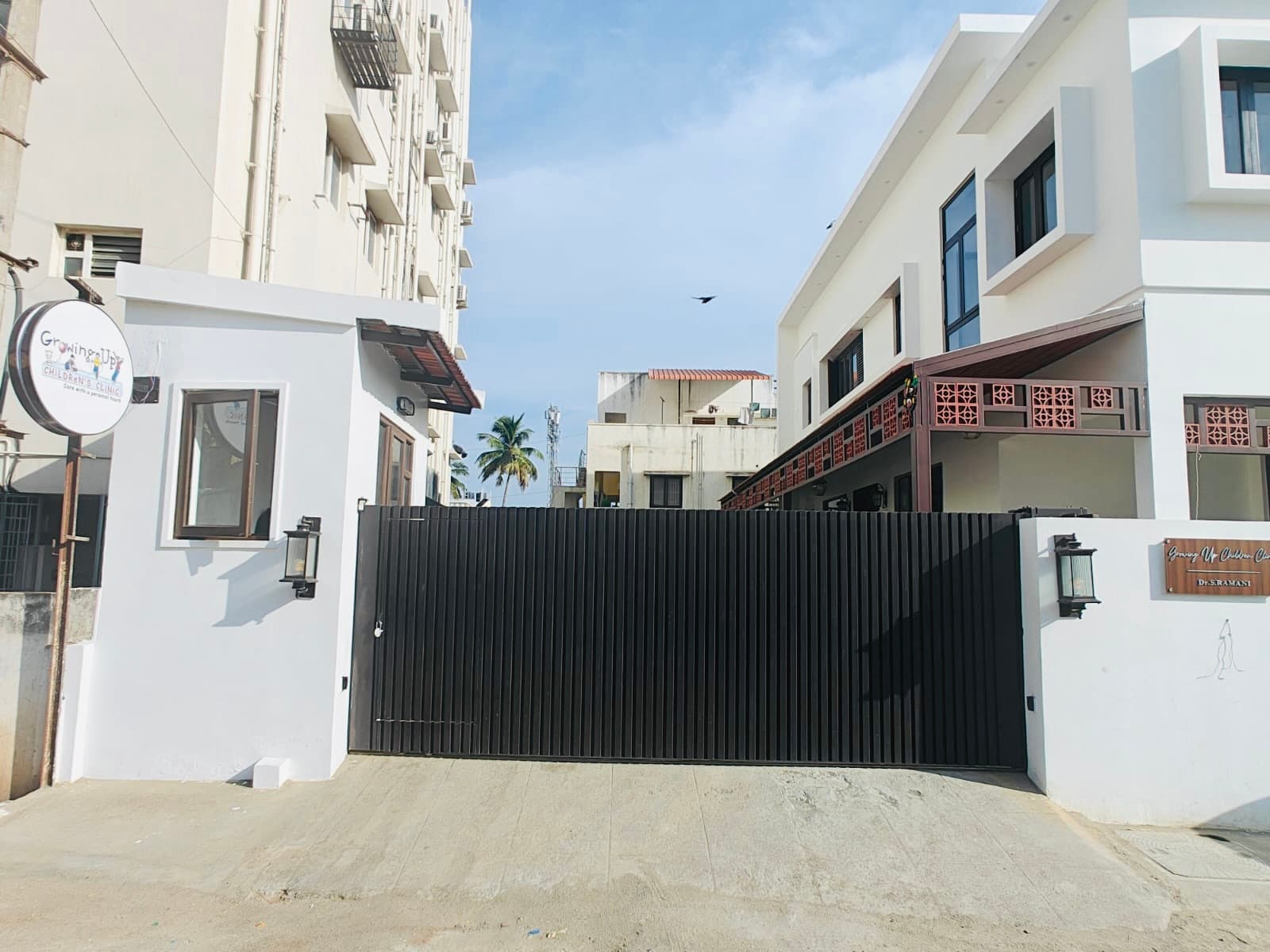 The dark sliding gate closed, with the round clinic sign above the compound wall