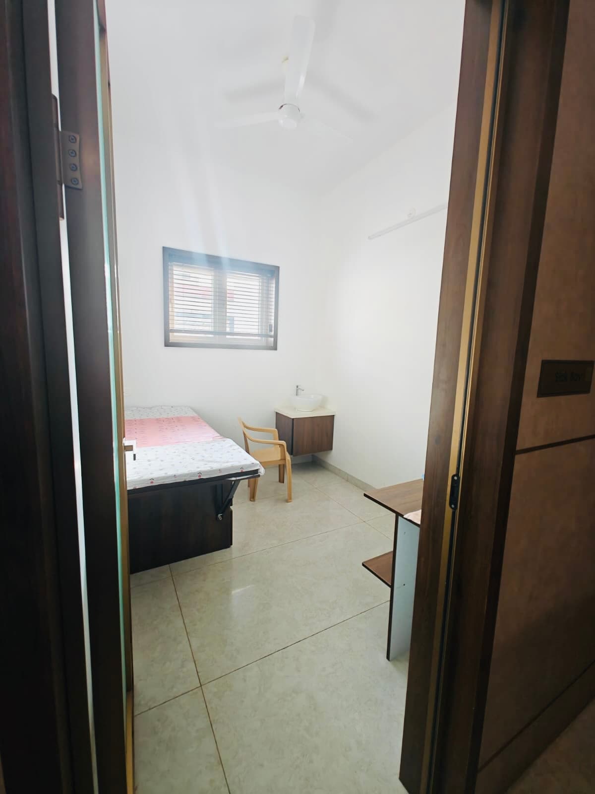 Inside the sick bay: a made bed, a chair and a washbasin under a shuttered window