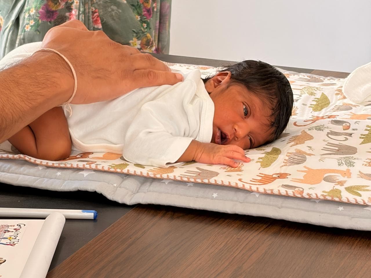 A newborn lying on the animal-print changing mat under the doctor's steadying hand
