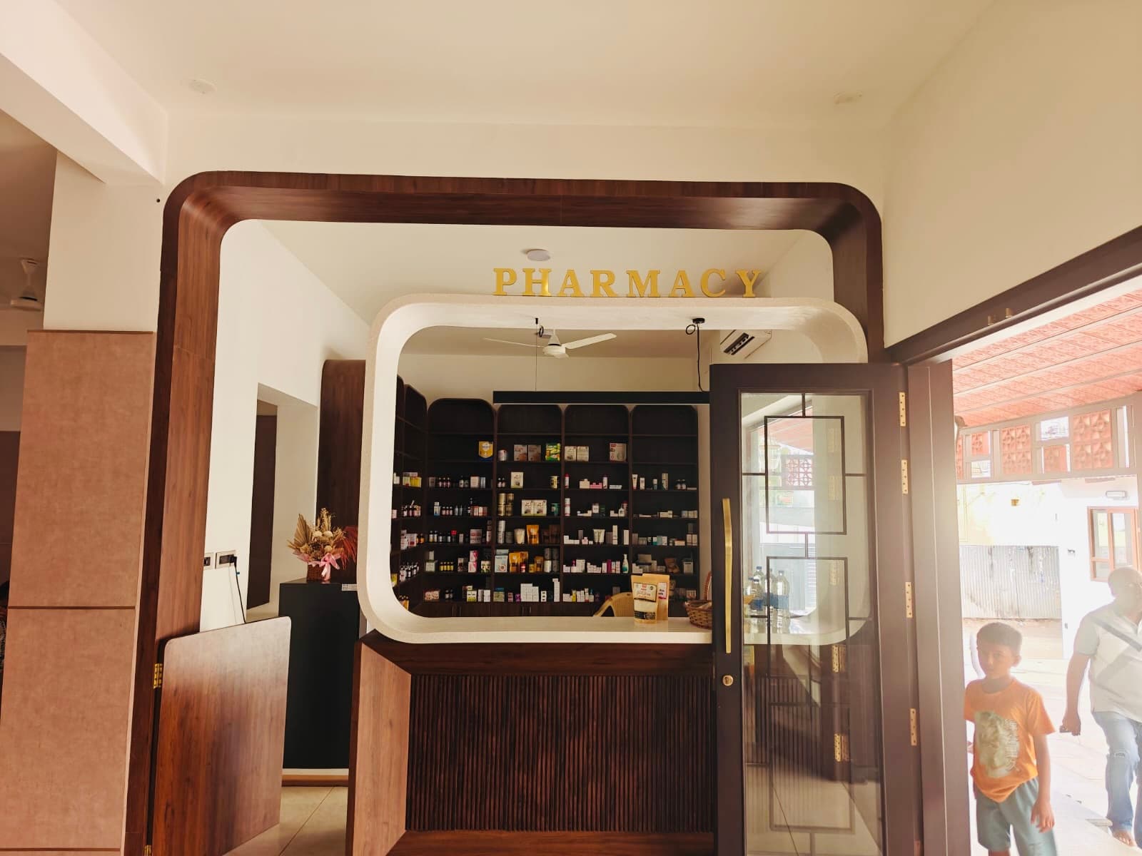 The clinic pharmacy counter in walnut and lime plaster, its shelves fully stocked