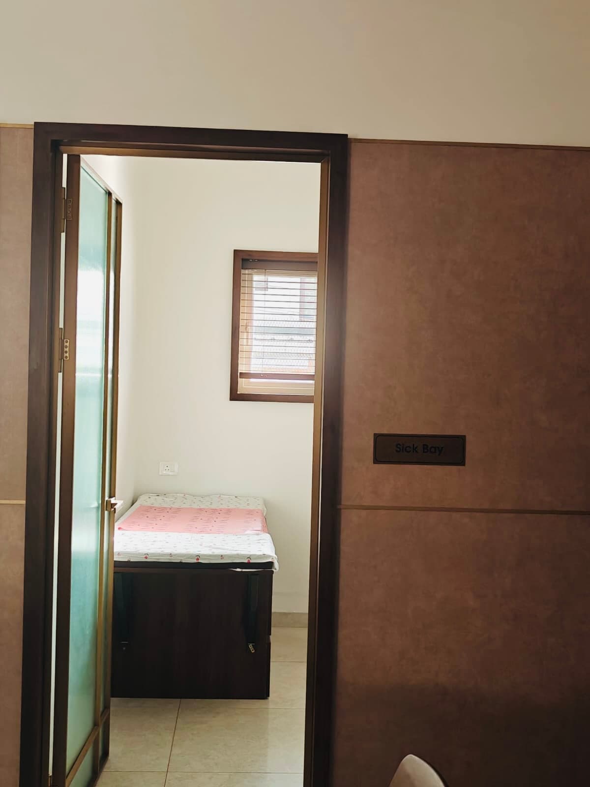 The Sick Bay door standing open onto a made-up bed under a shuttered window