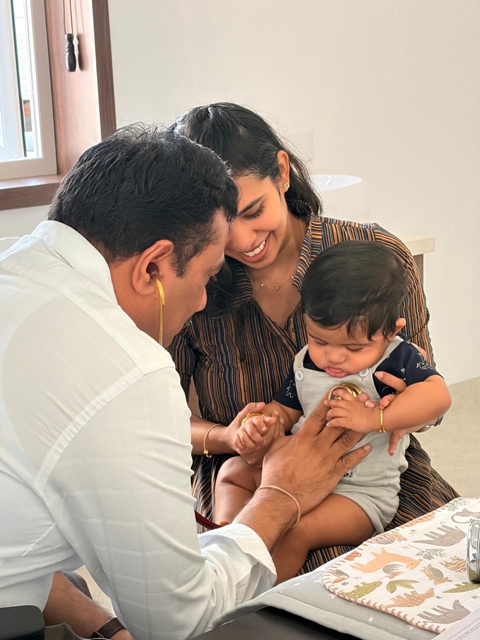 Dr. Ramani listening to a baby's chest while his mother holds him and smiles